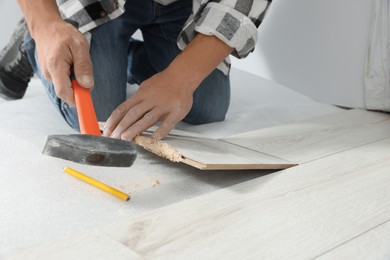 Photo of Professional worker using hammer during installation of new laminate flooring, closeup