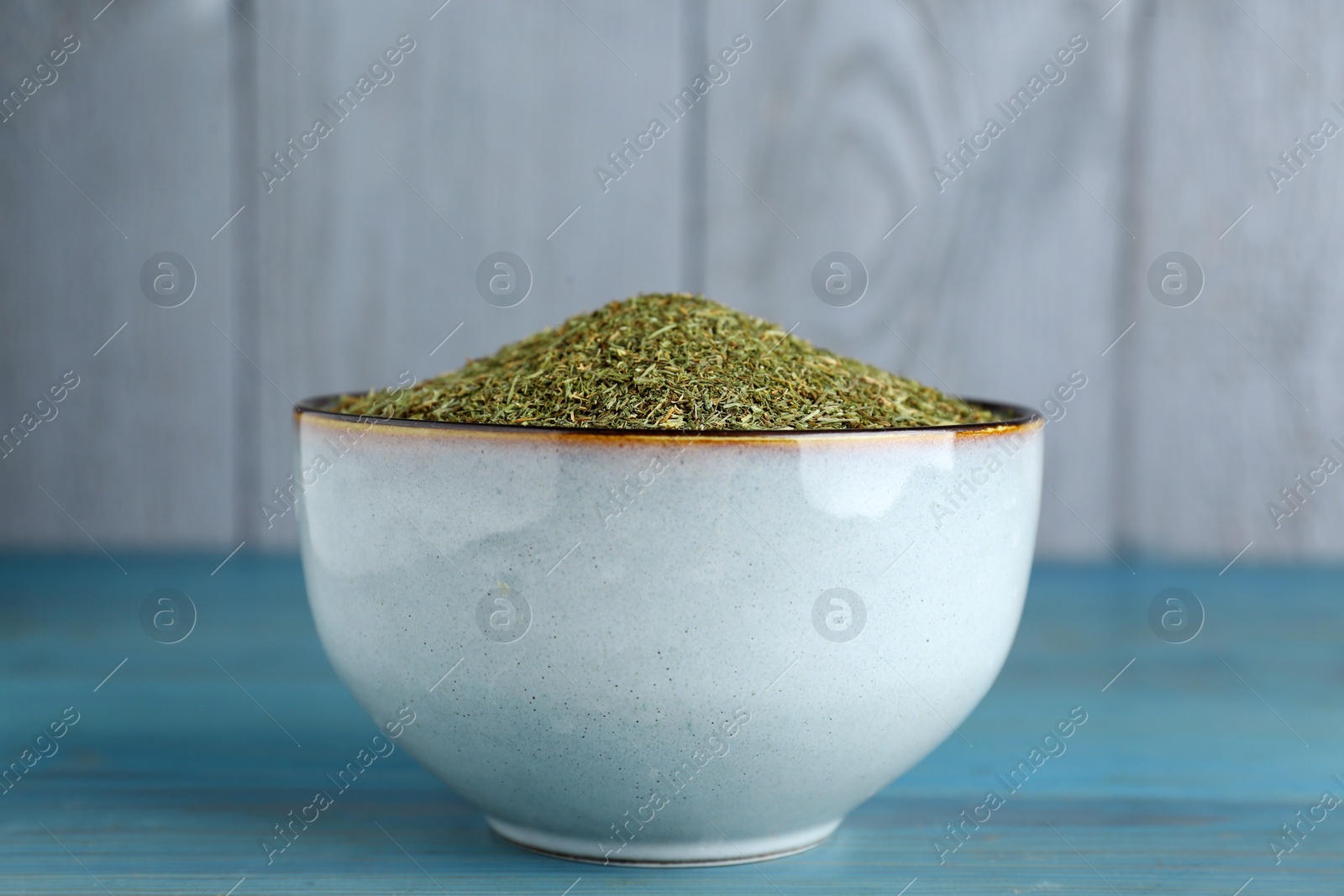 Photo of Dried dill in bowl on turquoise wooden table, closeup
