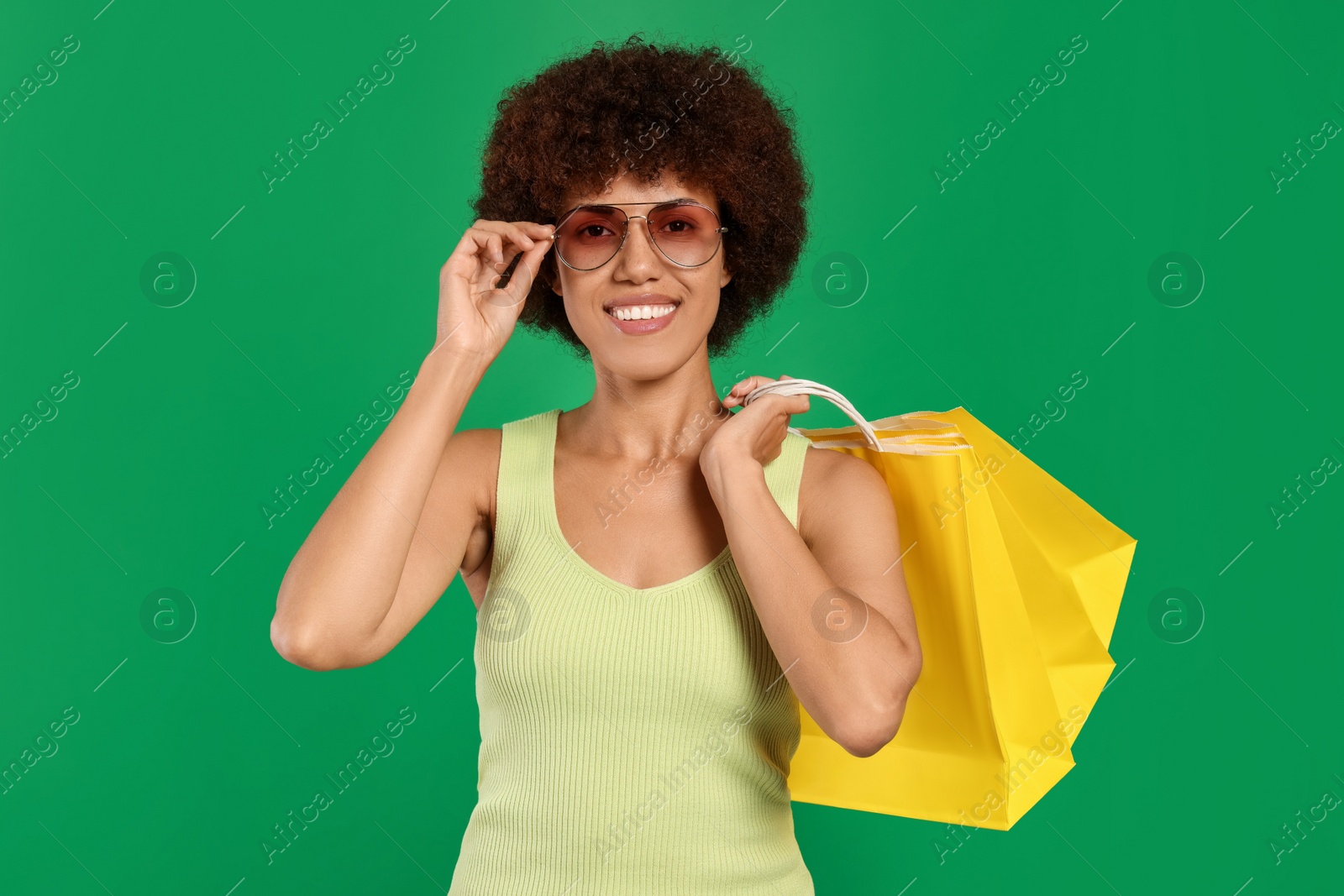 Photo of Happy young woman in sunglasses with shopping bags on green background