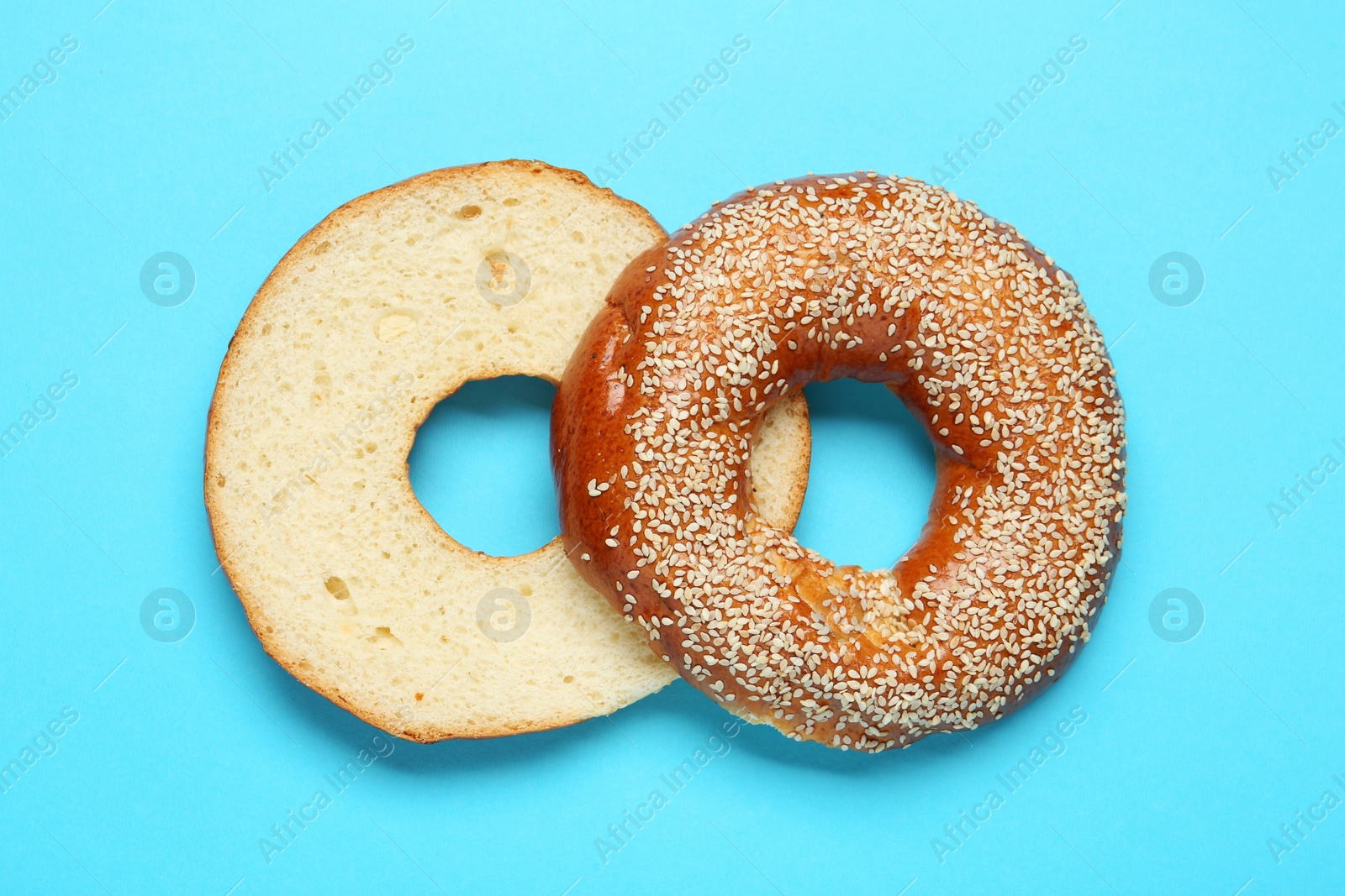 Photo of Delicious fresh halved bagel on light blue background, flat lay
