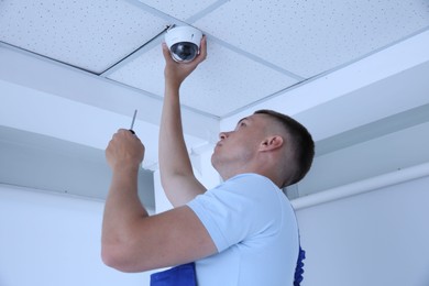 Photo of Technician with screwdriver installing CCTV camera on ceiling indoors