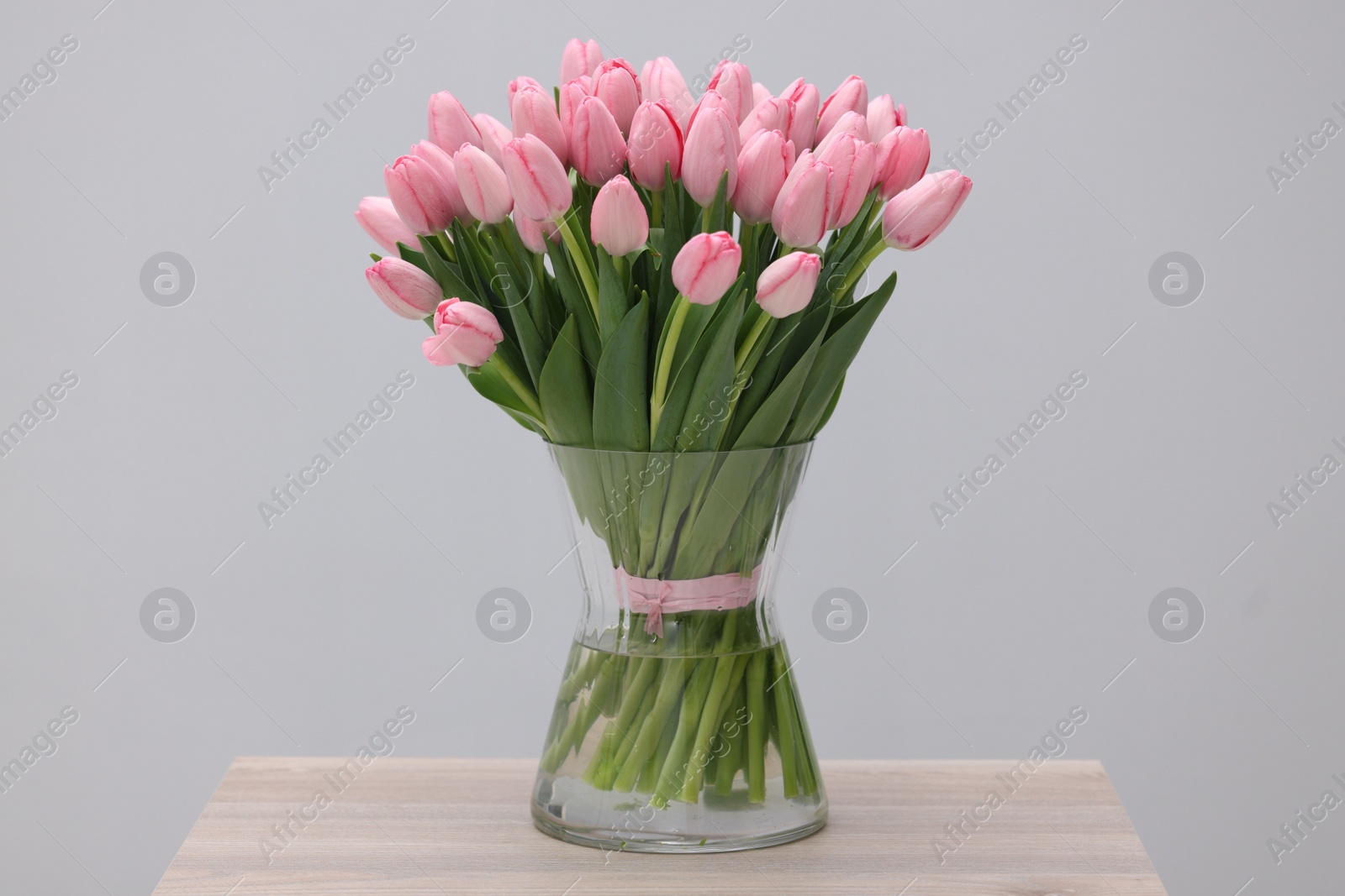 Photo of Bouquet of beautiful pink tulips in vase on wooden table against grey background