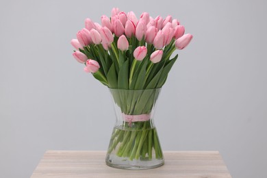 Bouquet of beautiful pink tulips in vase on wooden table against grey background