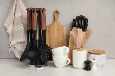 Set of different kitchen utensils and cups on white near gray wall