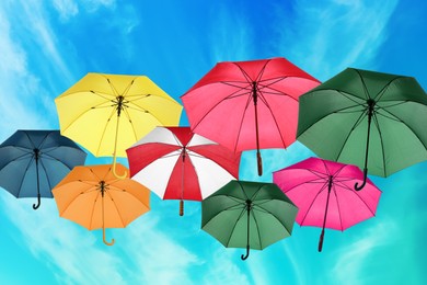 Image of Group of different colorful umbrellas against blue sky with white clouds on sunny day