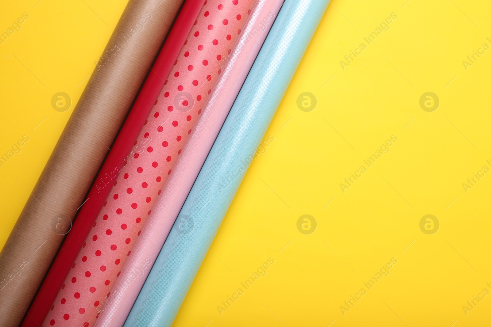 Photo of Rolls of colorful wrapping papers on yellow background, flat lay. Space for text