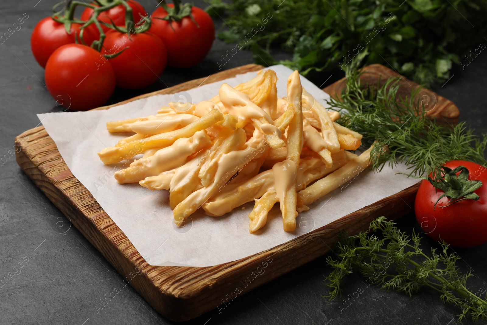 Photo of Delicious French fries with cheese sauce, tomatoes and dill on black table, closeup