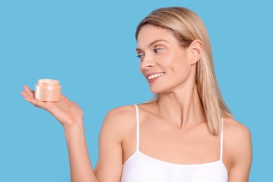 Woman with jar of body cream on light blue background