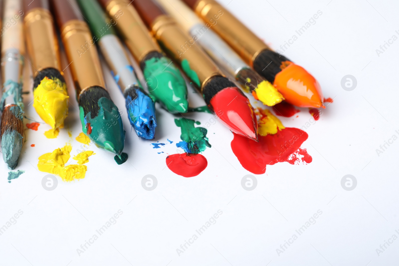 Photo of Brushes with colorful paints on white background, closeup