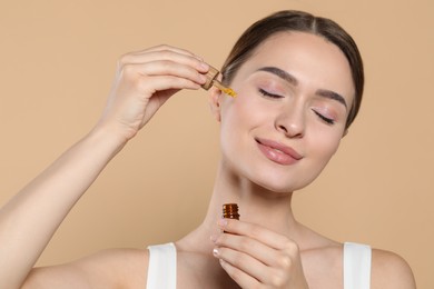 Young woman applying essential oil onto face on beige background