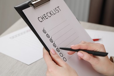 Photo of Woman filling Checklist at wooden table indoors, closeup