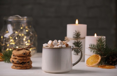 Cup of hot drink with marshmallows and cookies on white table