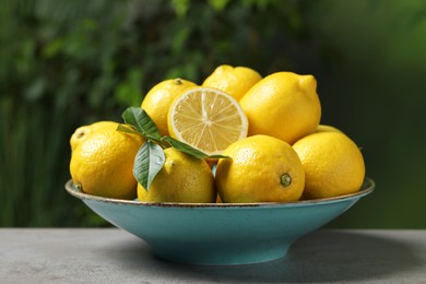 Photo of Fresh lemons and green leaves on grey table outdoors