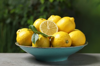 Fresh lemons and green leaves on grey table outdoors