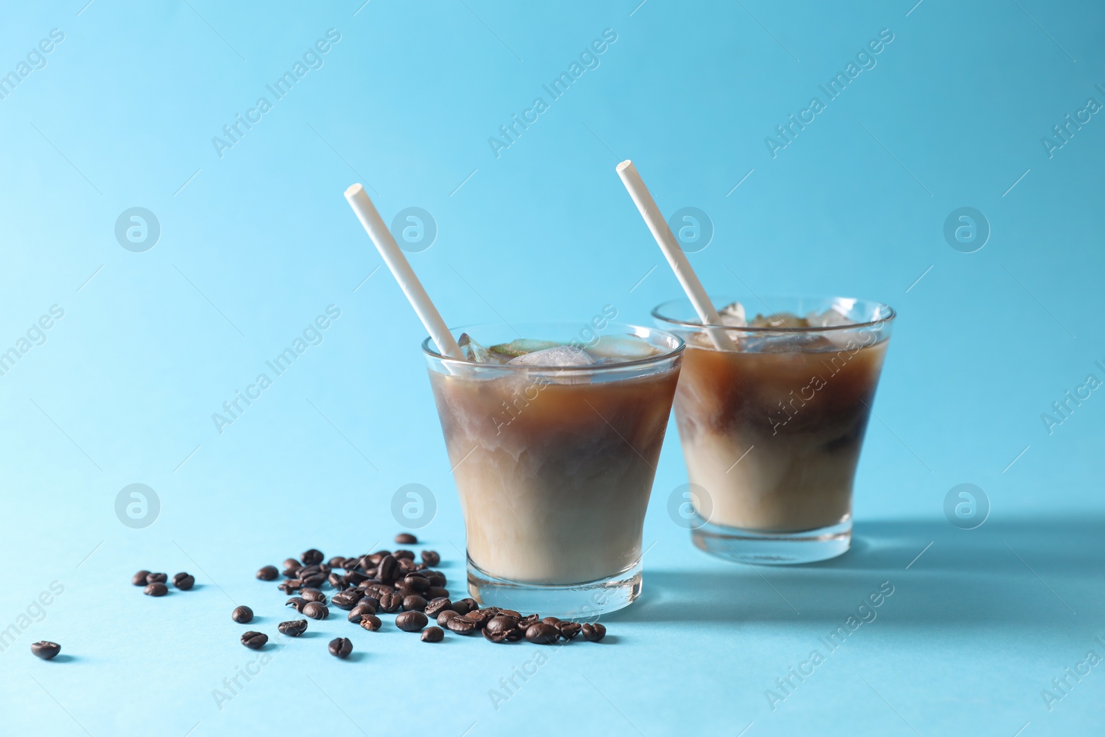 Photo of Refreshing iced coffee with milk in glasses and beans on light blue background