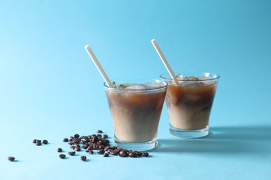 Refreshing iced coffee with milk in glasses and beans on light blue background