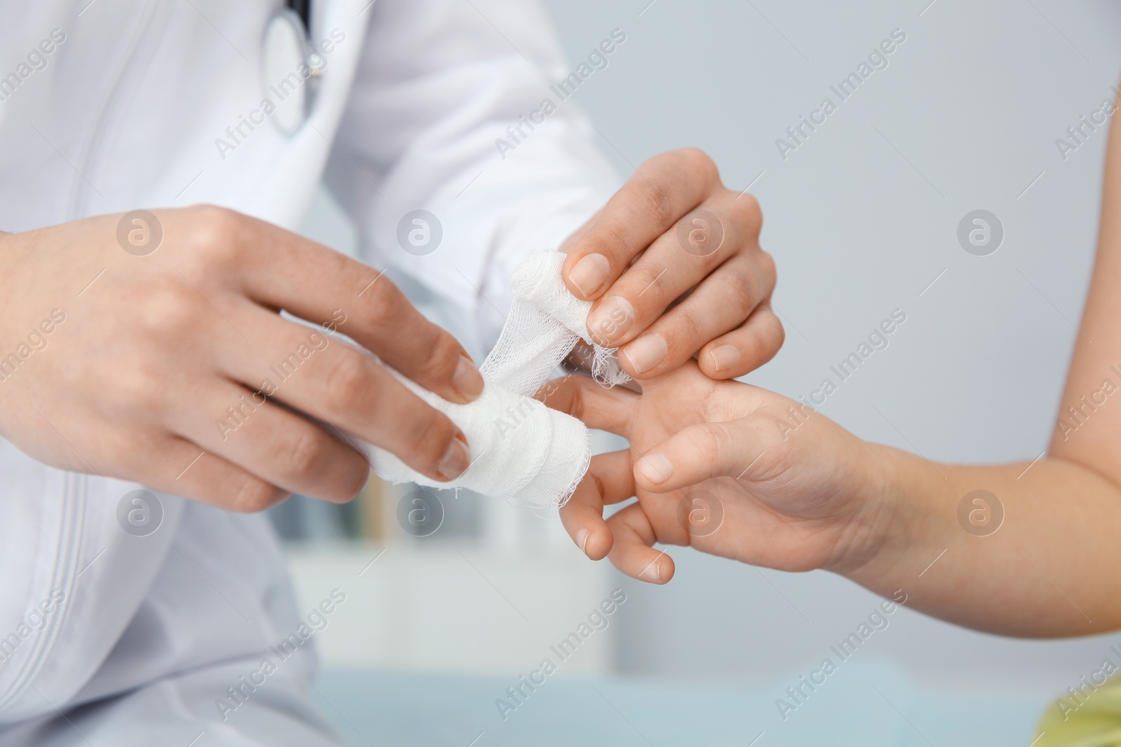 Photo of Female doctor applying bandage on little child's finger in clinic, closeup. First aid