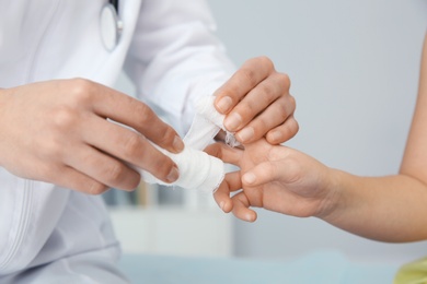 Female doctor applying bandage on little child's finger in clinic, closeup. First aid