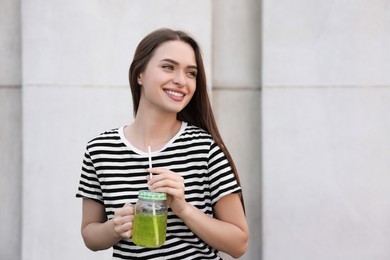 Young woman with mason jar of fresh juice outdoors, space for text