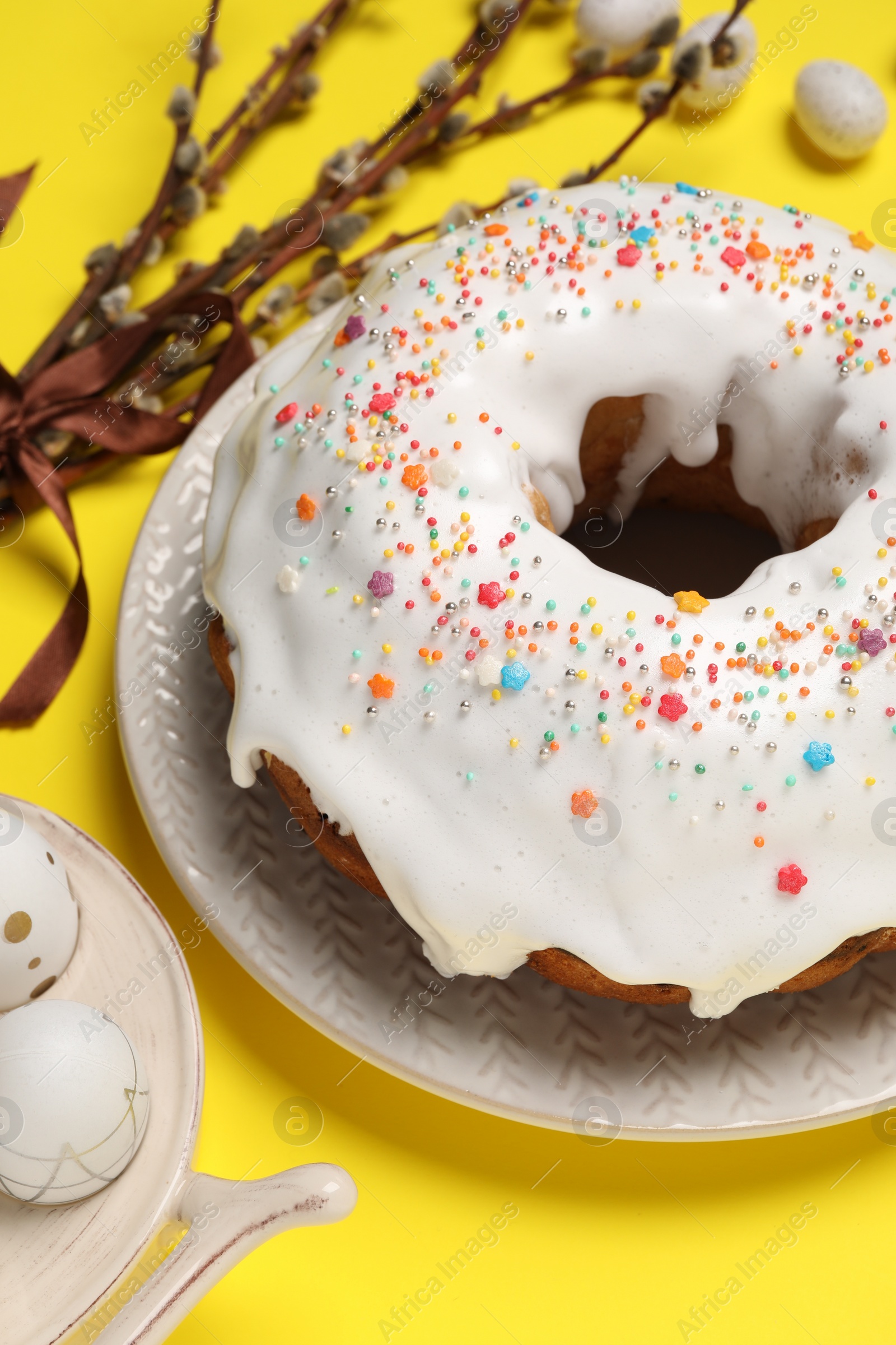 Photo of Easter cake with sprinkles, painted eggs and willow branch on yellow background