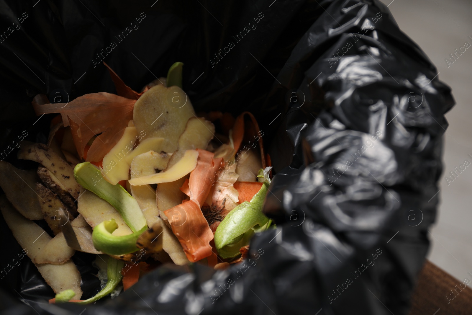 Photo of Garbage bin with peels of fresh vegetables indoors, closeup