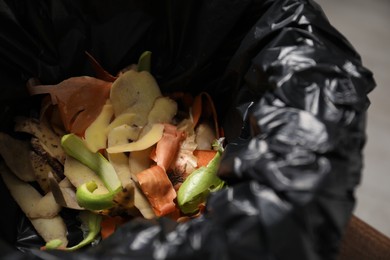 Photo of Garbage bin with peels of fresh vegetables indoors, closeup