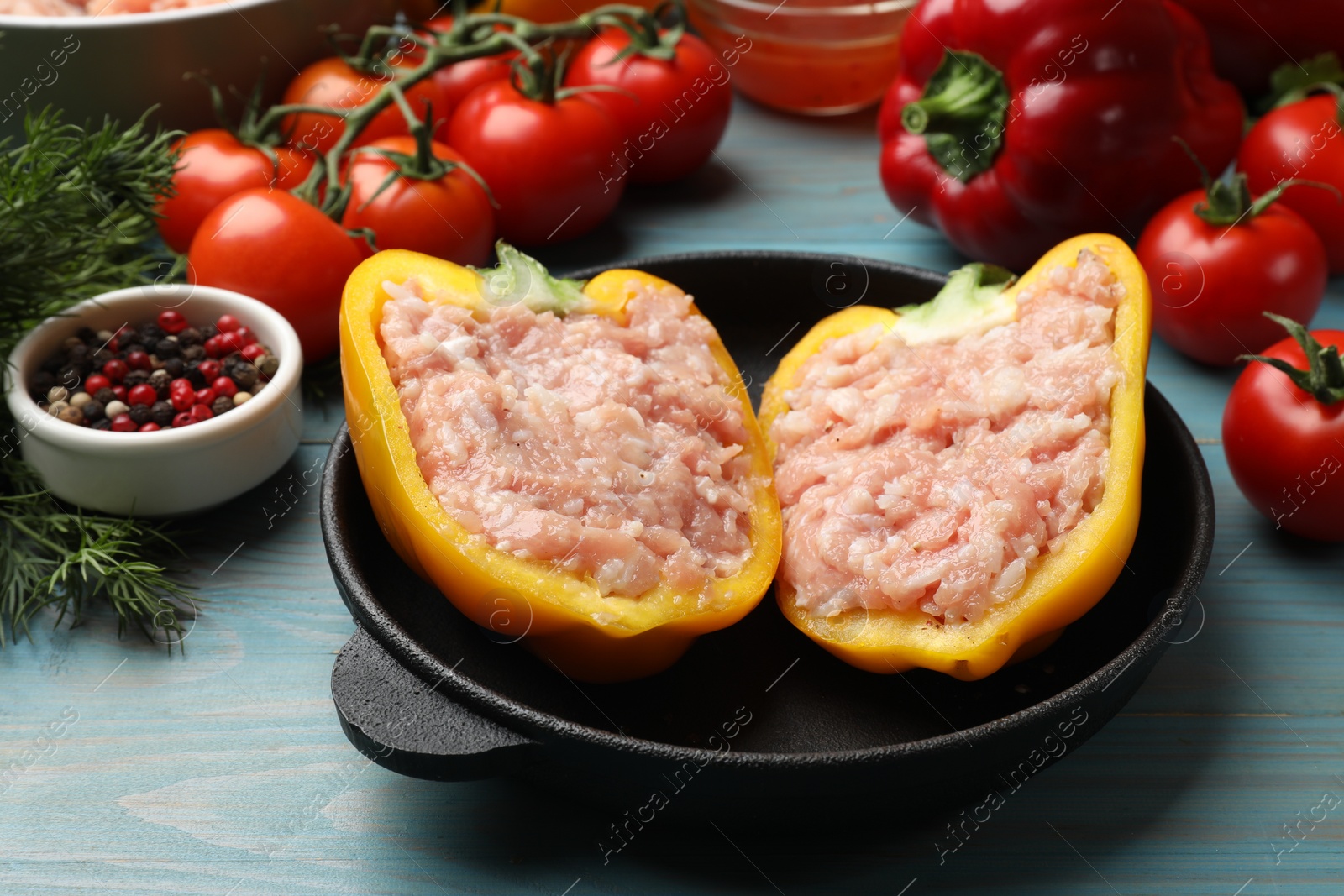 Photo of Raw stuffed peppers with ground meat and ingredients on light blue wooden table