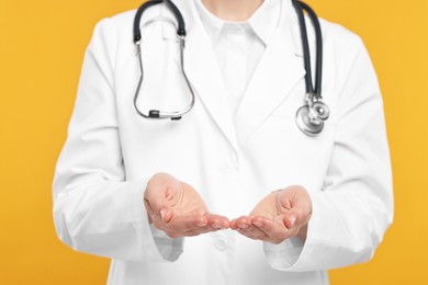 Doctor with stethoscope holding something on orange background, closeup