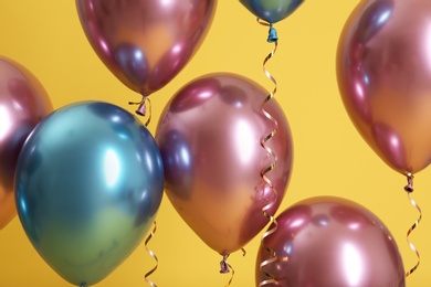 Bright balloons with ribbons on color background