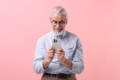 Photo of Portrait of stylish grandpa with glasses using smartphone on pink background
