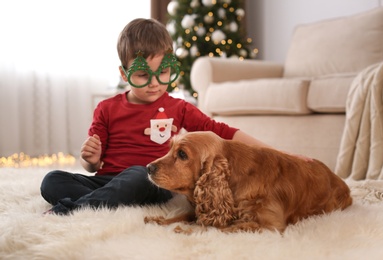 Photo of Cute little boy with English Cocker Spaniel in room decorated for Christmas