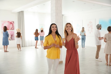 Young women with glasses of champagne at exhibition in art gallery