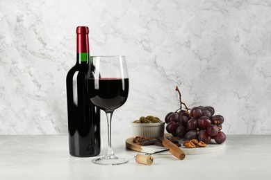 Delicious red wine, corkscrew and snacks on table against white marble background