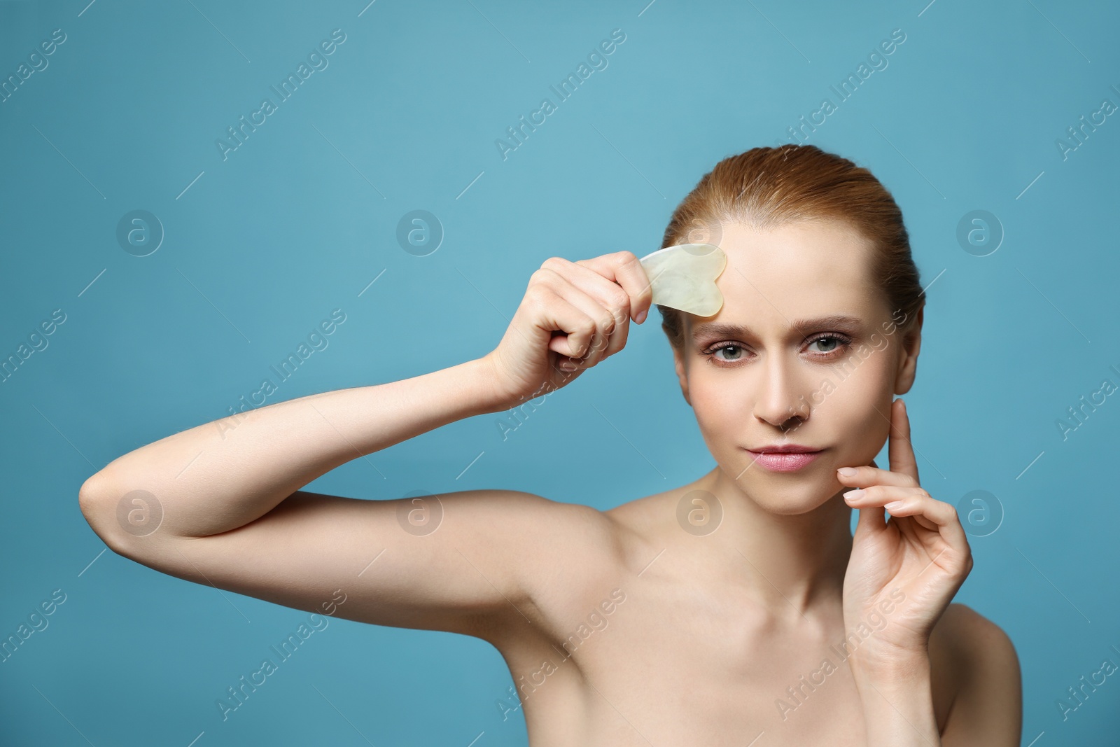 Photo of Beautiful young woman doing facial massage with gua sha tool on blue background