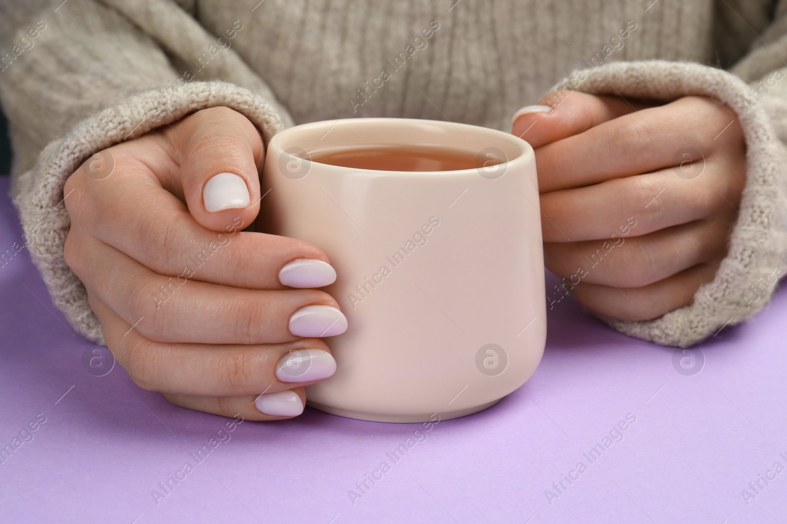 Photo of Woman with white polish on nails holding cup of hot drink on violet background, closeup