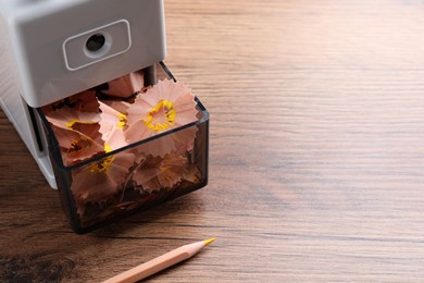 Photo of Mechanical sharpener with pencil shavings on wooden table. Space for text