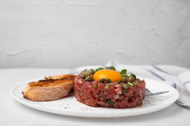 Photo of Tasty beef steak tartare served with yolk, capers and toasted bread on white table