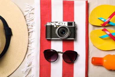 Photo of Hat, sunglasses, camera, sunscreen, beach towel and flip flops on sand, flat lay