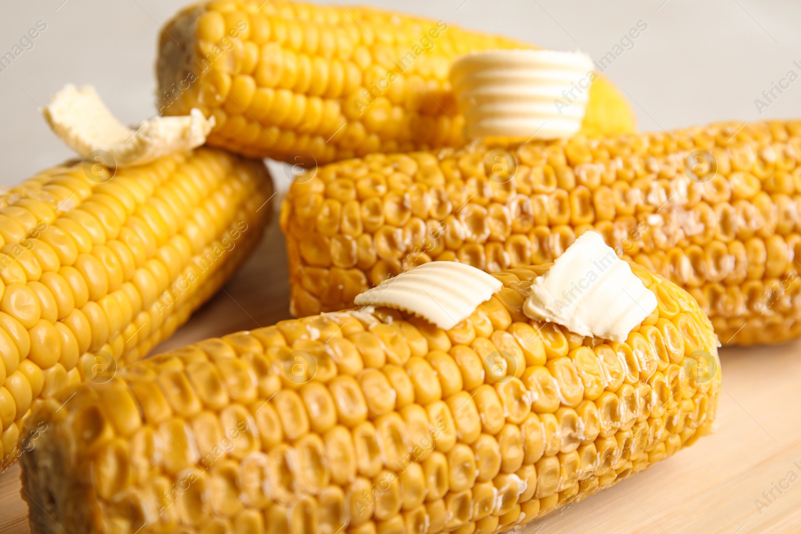 Photo of Delicious boiled corn with butter on wooden board, closeup