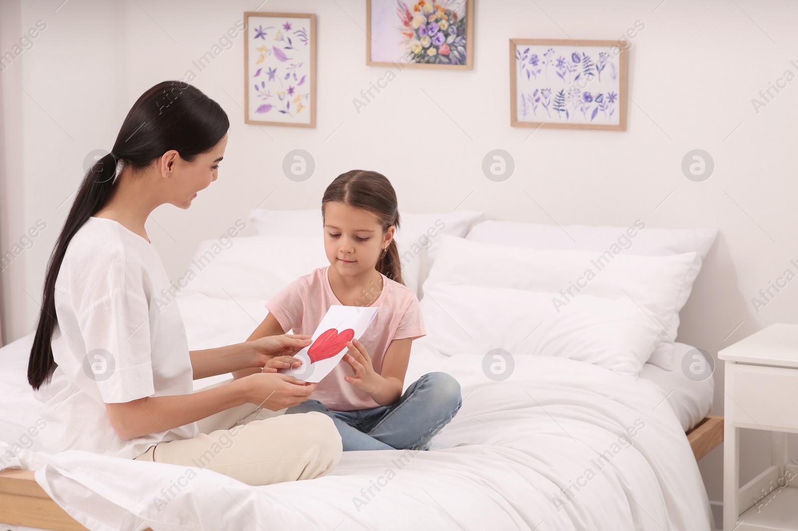 Photo of Daughter gifting happy woman handmade greeting card on bed at home. Mother's day celebration