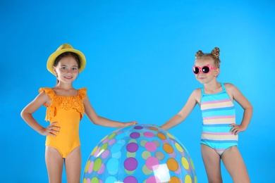Cute little children in beachwear with inflatable ball on light blue background