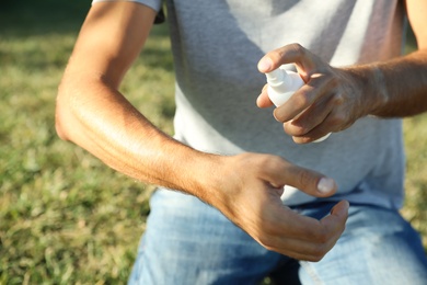 Photo of Man applying insect repellent onto arm outdoors, closeup