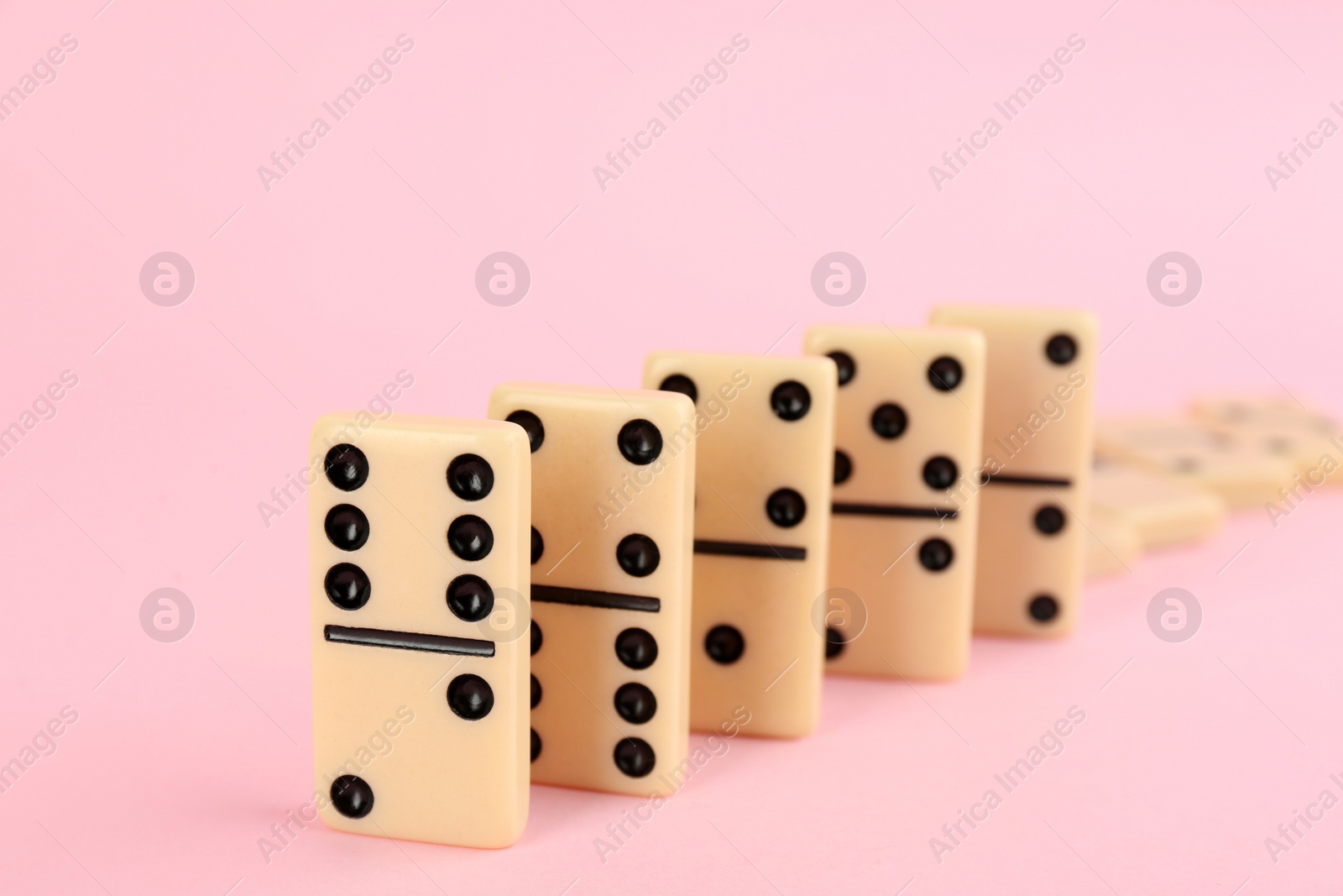 Photo of White domino tiles falling on pink background