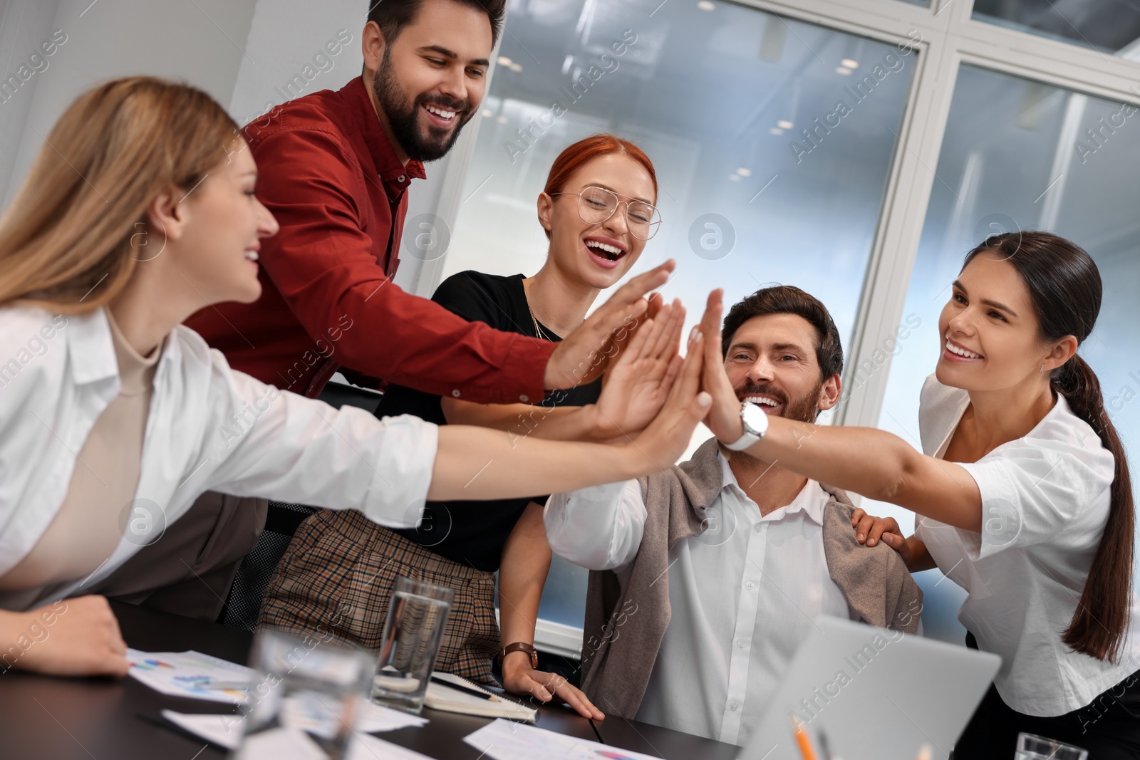 Photo of Team of employees joining hands in office