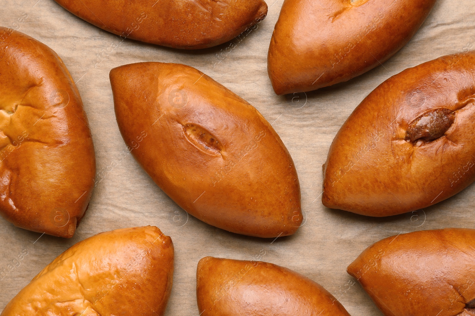 Photo of Many delicious baked patties on parchment paper, flat lay