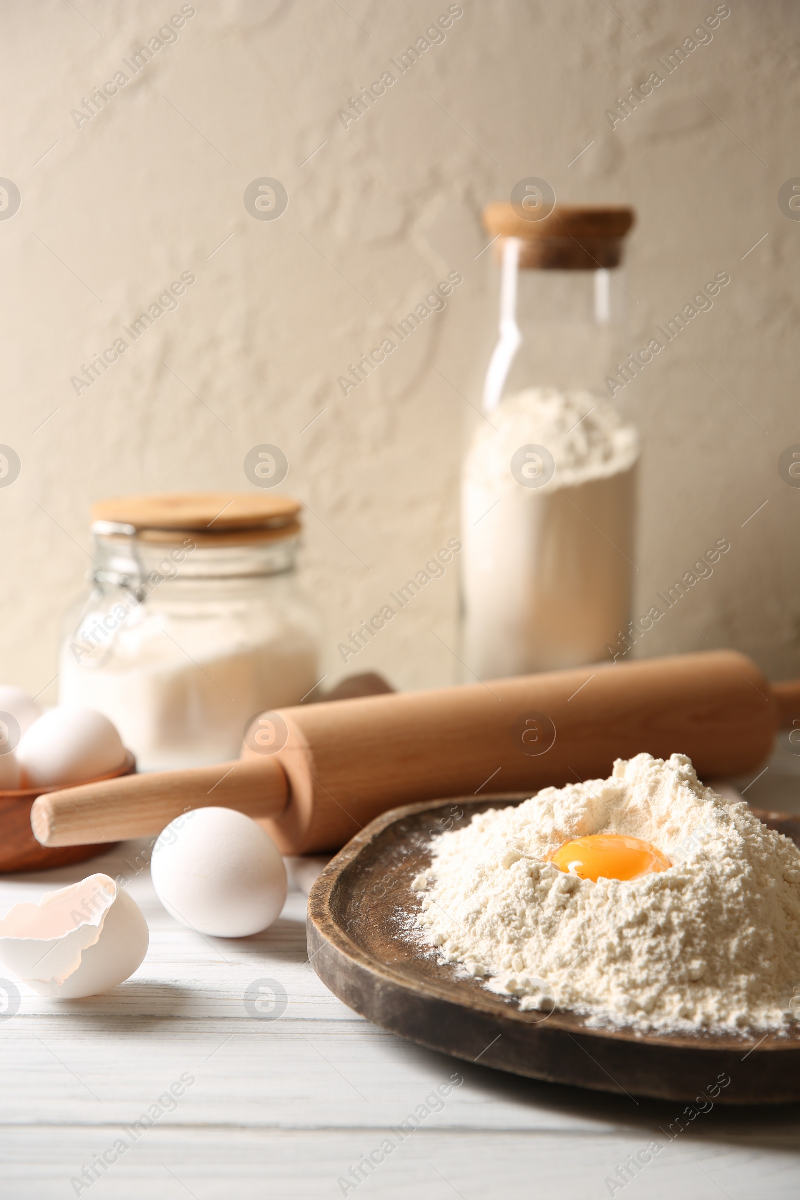 Photo of Making dough. Pile of flour with yolk, rolling pin and eggs on white wooden table, closeup