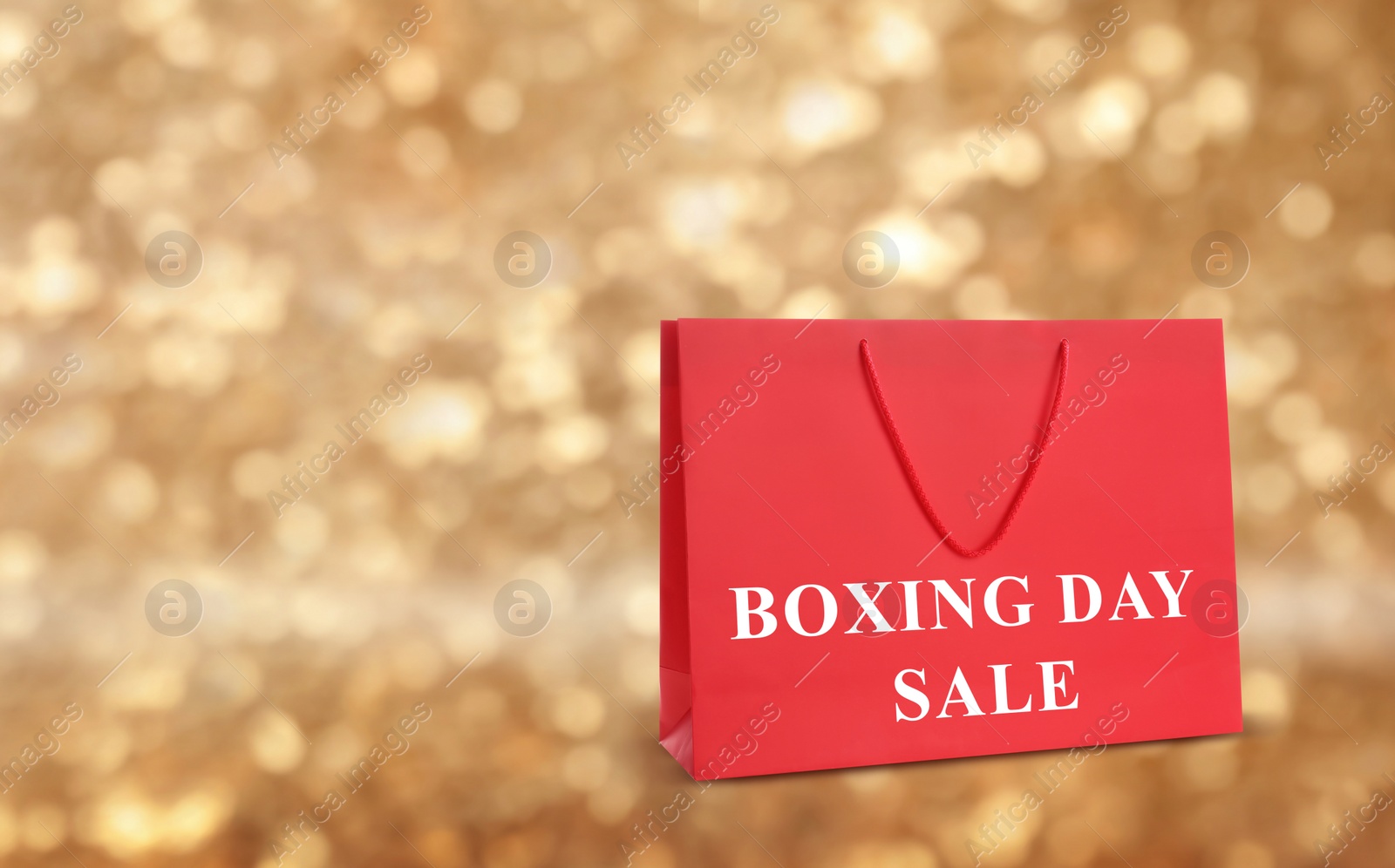 Image of Red shopping bag with text Boxing Day Sale on blurred gold background, closeup. Space for text