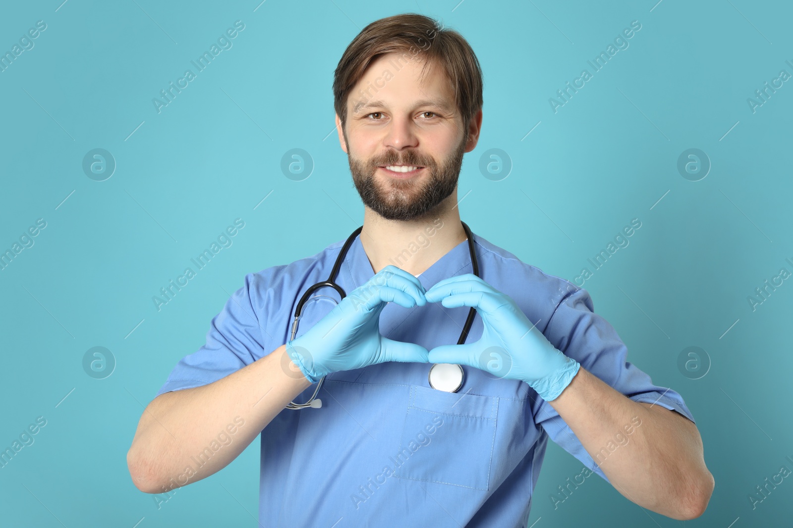 Photo of Doctor or medical assistant (male nurse) making heart with hands on turquoise background