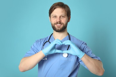 Photo of Doctor or medical assistant (male nurse) making heart with hands on turquoise background