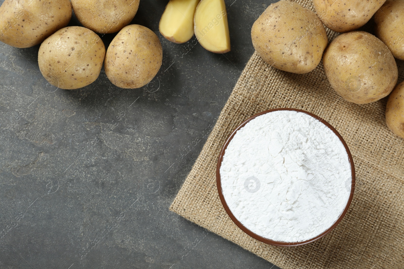 Photo of Bowl with starch and fresh potatoes on grey table, flat lay